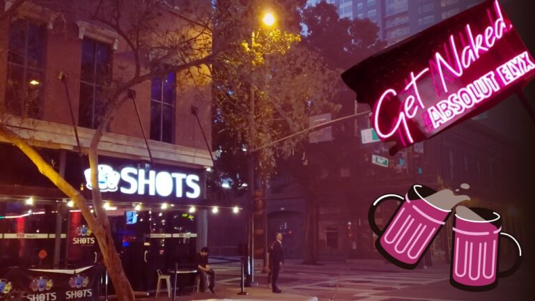 Exterior view of a bar named "Shots" in downtown Orlando, illuminated by neon signs, including one that says "Get Naked.